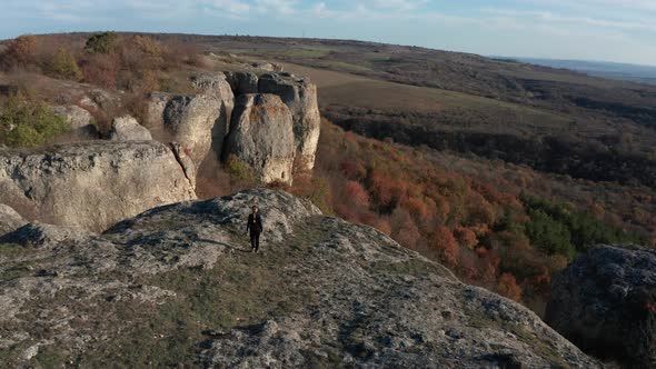 Rear view of a young blonde woman, walking along the edge of stunning rock formation