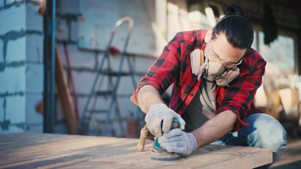 A Young Man in a Construction Respirator Grinds a Parquet Board with a Sander