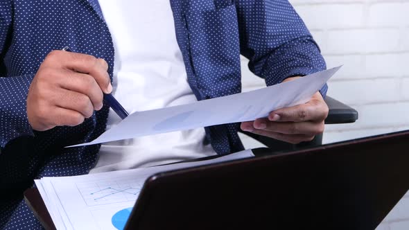 Young Man Sitting on a Chair Analyzing Financial Data on Paper