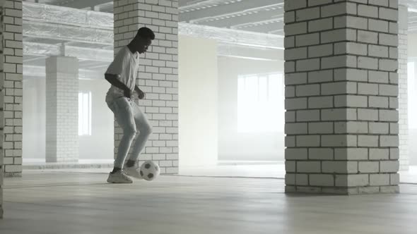 Young Black Guy Trains with a Soccer Ball at Indoors