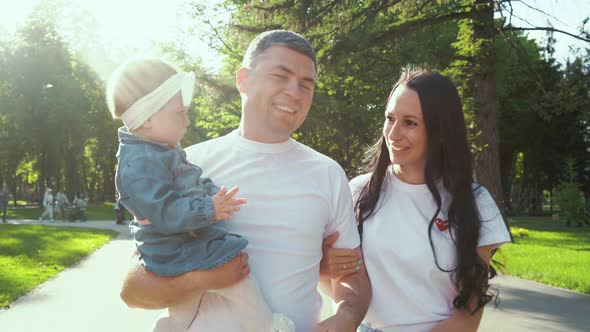 Happy Family with Toddler Girl Walking in Sunny Park in Summer with Lens Flare Effect