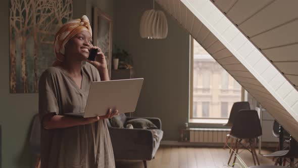 Young Black Woman with Laptop Making Phone Call at Home