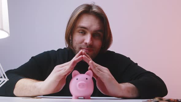 Young Man Making Roof Over the Piggy Bankk with His Hands