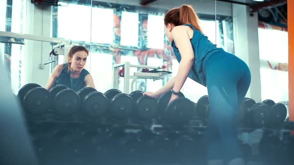 Wide Frame-young Fitness Girl Performs an Exercise with a Dumbbell in Front of a Huge Mirror