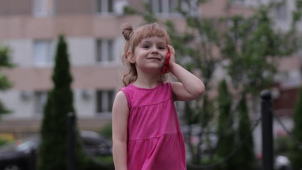 Child Girl Talking By Smartphone Outdoors. Kid in Pink Dress Talking By Mobile Phone on City Street