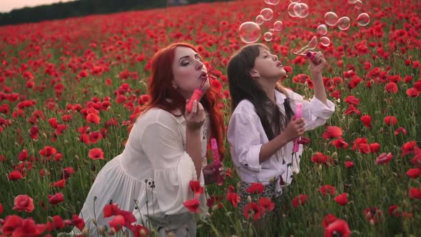 Happy Little Girl and Her Mom Blow Soap Bubbles in Blooming Field of Red Poppies Slow Motion