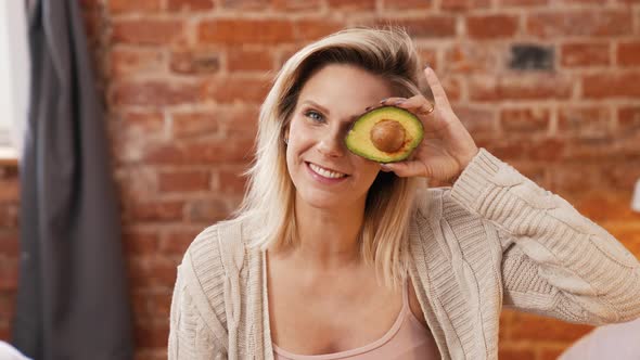 Happy Smiling Caucasian Blond Woman Holding a Half of Avocado in Front of Her Eye