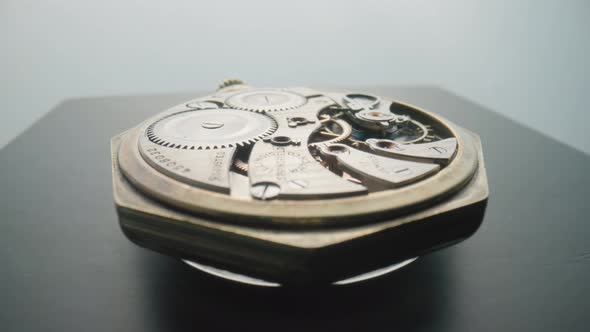 An Antique Pocket Watch with an Open Working Clock Mechanism Rotates on a Gray Table in a Studio