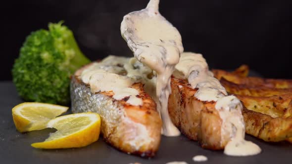 Grilled salmon steak pouring topping cream sauce and rotate on a black background with lemon slice