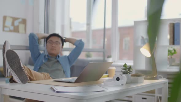 Asian Office Worker Resting with Legs on Office Desk