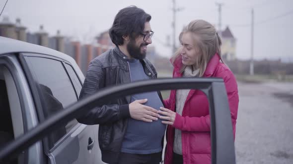 Smiling Caucasian Blond Woman Caressing Her Husband's Pregnant Belly and Imitating Listening Baby