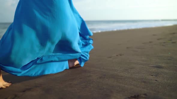 Legs of a Woman in Beautiful Blue Dress Walking Along a Black Volcanic Beach