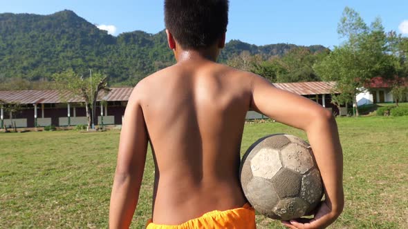 Back Of Rural Boy Walking With Old Soccer Ball