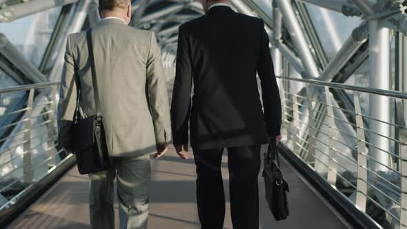 Successful Business Men Walking Along Glass Bridge