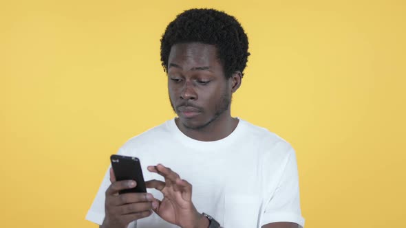 African Man Excited for Success on Smartphone Yellow Background