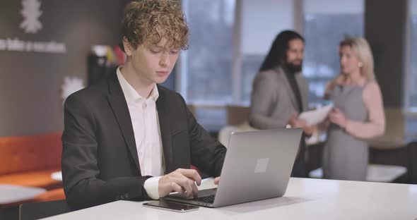 Portrait of Young Caucasian Man with Curly Hair Typing on Laptop Keyboard. Portrait of Confident