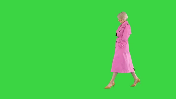 Trendy Beautiful Senior Woman in a Pink Coat Walks in and Showing Her Outfit To Camera on a Green