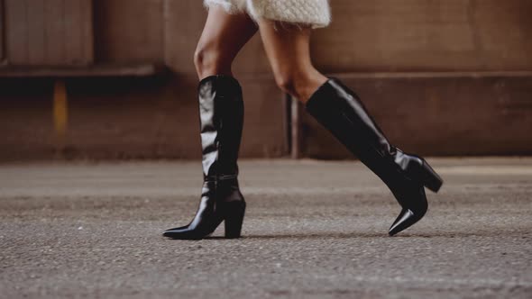 Young Woman In Black Leather Boots Walking Along Street