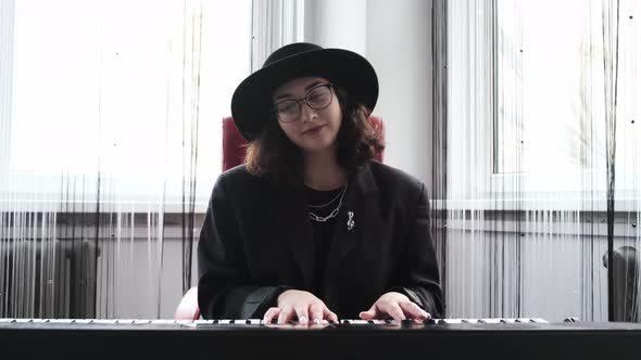 A Young Girl in a Hat is Practicing Piano in the Studio