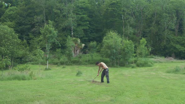 Topless man rakes hay in field alone