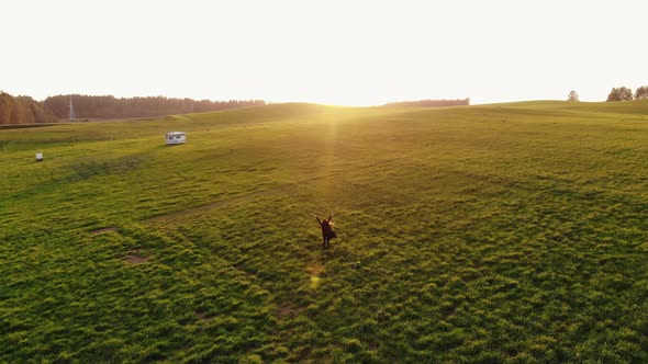 Shooting From Drone of a Young Girl Who Walks Through Hilly Meadows and Spinning Raising Her Hands