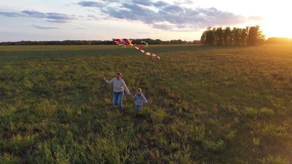 The Mother and Boy Run with a Kite on a Green Field