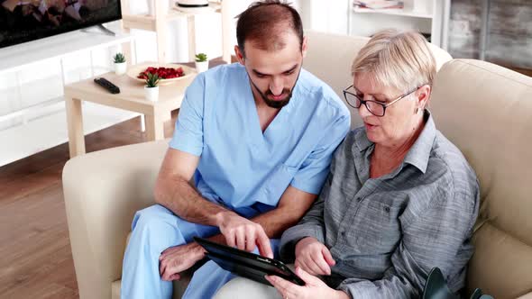 Male Nurse Teaching Elderly Old Woman How To Use Her Tablet PC