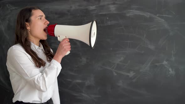 Beautiful Girl Student Stands Near the Chalk Board Holds a Megaphone in Her Hands and Yells