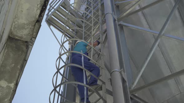 Bottom View of Male Caucasian Worker Climbing Up the Ladder on Huge Metal Tower. Confident