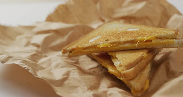 Video of close up of toasted cheese sandwiches on brown paper over grey background