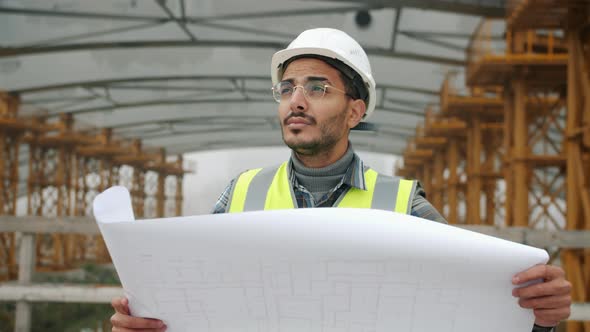 Portrait of Middle Eastern Construction Employee Wearing Uniform Studying Blueprint Outdoors