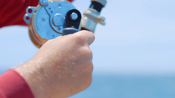 Fisherman reeling in big fish, close up on hand turning reel crank handle