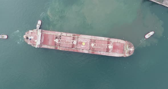 Large cargo ship enters the port escorted by tugboats.