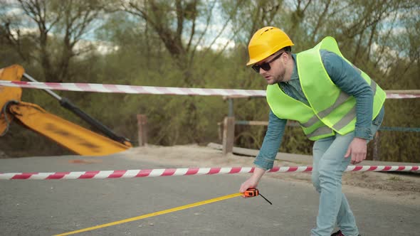 Bearded Engineer in Protective Helmet Tape Measure in Hands Measures Distance