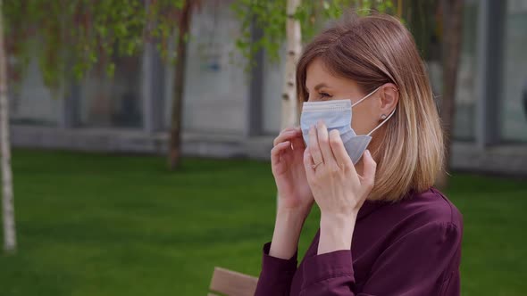 Portrait young woman putting on medical mask standing outdoor in town.