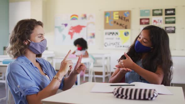 Female teacher and girl wearing face masks talking to each other through sign language in class