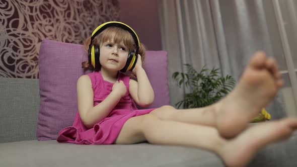 Little Child Girl in Headphones Enjoying Listen Music. Dancing on Sofa at Home