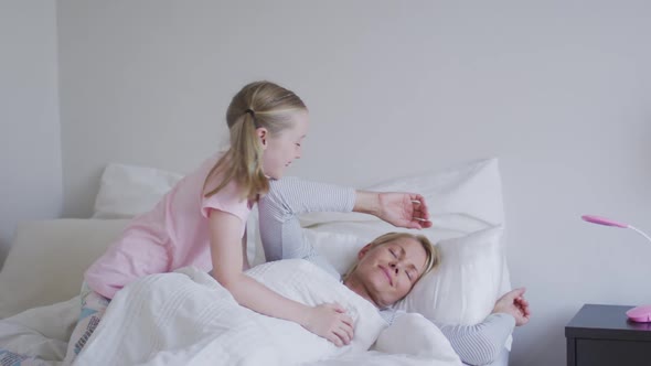 Side view of Caucasian girl waking up her mother on bed