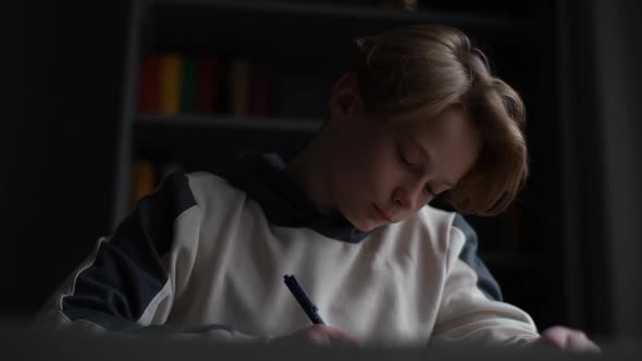 Closeup Face of Concentrated Pupil Boy Writing Notes in Paper Workbook Sitting at Desk in Classroom