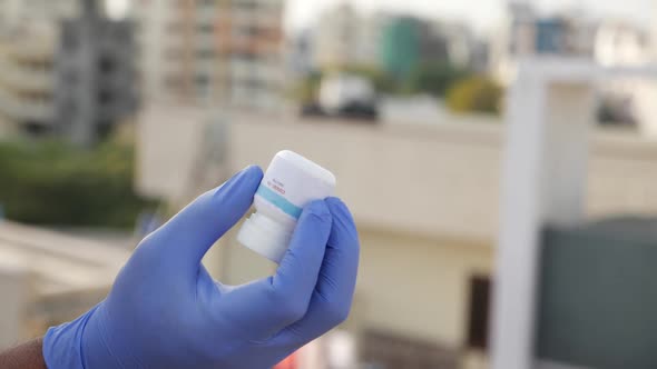 Man with blue gloves holding covid-19 vaccine tablets bottle