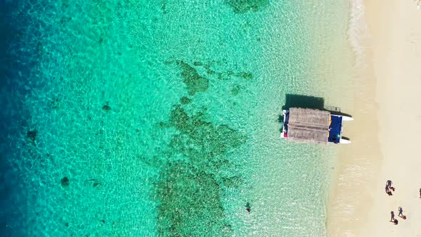 Traditional boat with straw roof anchoring on sandy beach washed by calm clear water of blue turquoi