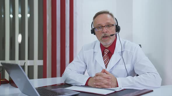 Online conference doctor at clinic. Handsome mature medical doctor consulting patient during video c