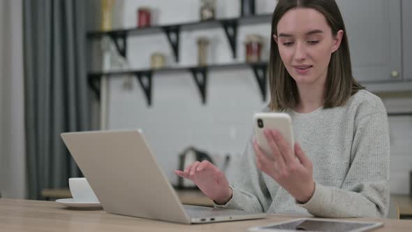 Young Woman Using Smartphone and Working on Laptop at Home