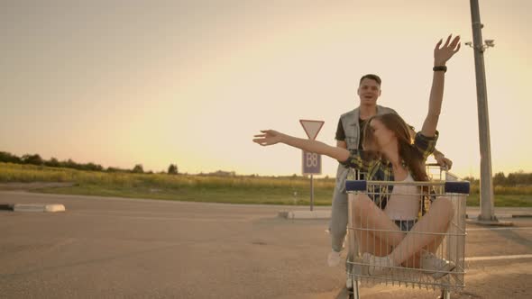 Side View of a Young Female and Male Having Fun Outdoors on Shopping Trolleys