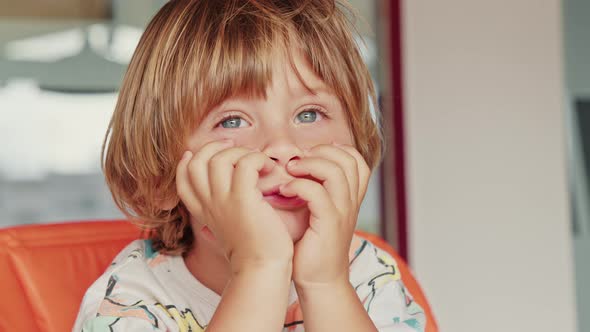 Portrait of a Little Lovely Kid Sitting in Orangecolored Chair in the Kitchen