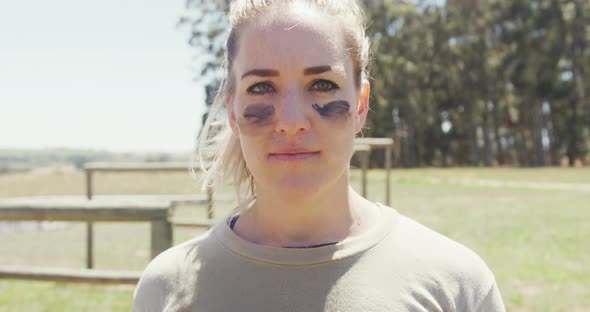 Portrait of confident female soldier wearing eye black standing in field on obstacle course alt