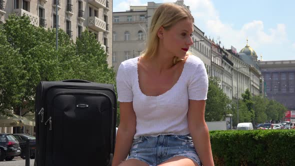 A Young Beautiful Woman with a Suitcase Looks Around an Urban Area with a Smile