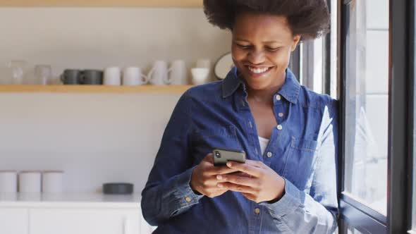 Happy african american woman using smartphone in kitchen
