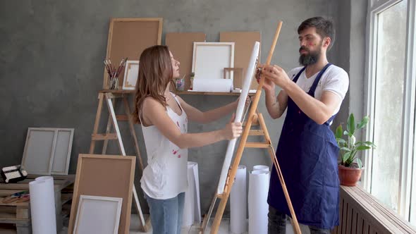 A Man and a Woman in an Art Studio Walk Up to the Easel and Fix the Canvas