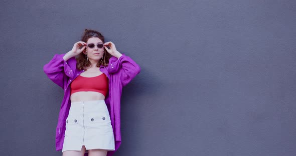the girl adjusts her sunglasses, laughs and poses near the wall. middle plan